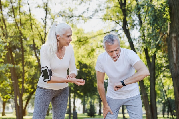 Hombre y mujer mayores cansados chequeando el pulso después de hacer ejercicio al aire libre