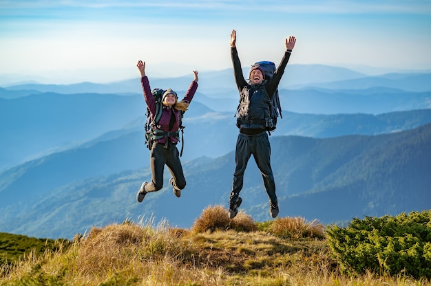 El hombre y una mujer con mochilas saltando en la montaña.