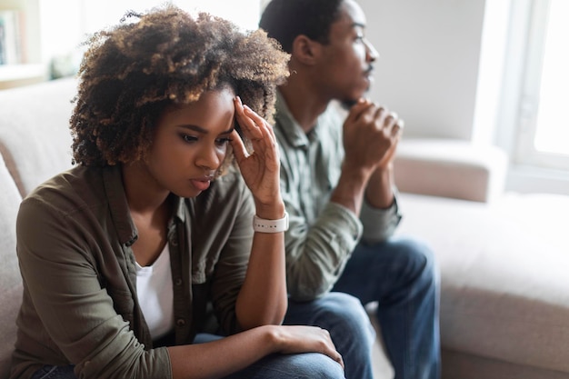 Un hombre y una mujer negros infelices sentados en un sofá en casa