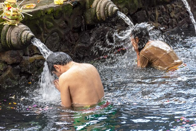 Hombre y mujer orando y ritual de purificación en el templo de Pura Tirta Empul de agua de manantial sagrado