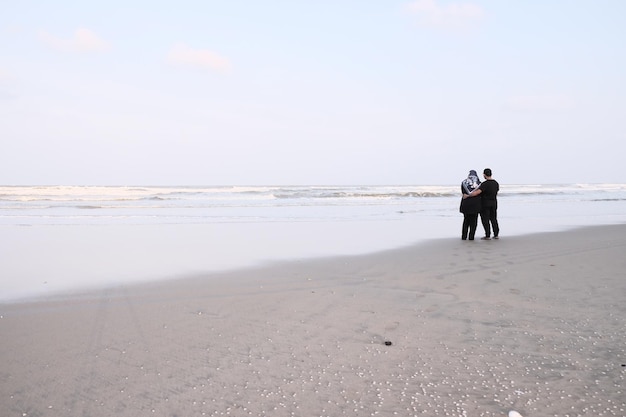 Un hombre y una mujer se paran en la playa y miran el océano.