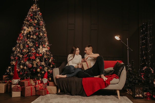 Hombre y mujer pareja enamorada abrir cajas de regalo desatar un arco cerca del árbol de navidad