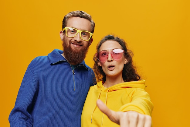 Hombre y mujer pareja sonriendo alegremente y torcidos con gafas sobre fondo amarillo símbolos signos y gestos con las manos familia disparar recién casados