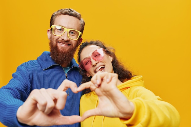 Hombre y mujer pareja sonriendo alegremente y torcidos con gafas sobre fondo amarillo símbolos signos y gestos con las manos familia disparar recién casados