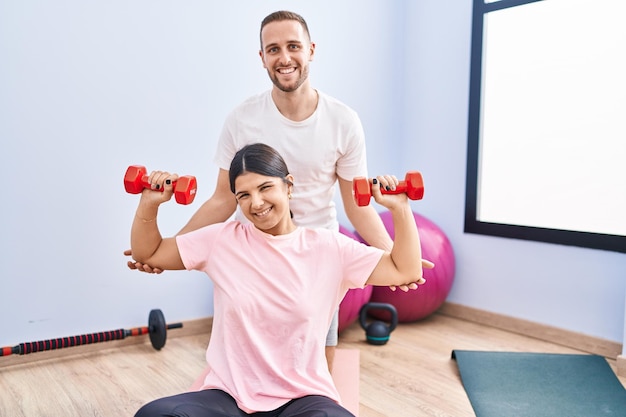 Hombre y mujer pareja sonriendo confiado entrenamiento usando pesas en el centro deportivo