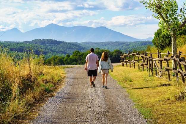 Hombre y mujer paseando por un camino de tierra entre olivares con las montañas al fondo y al atardecer