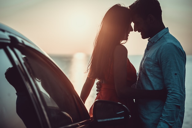 El hombre y la mujer de pie cerca del coche en la orilla del mar.