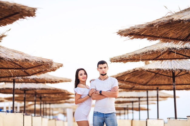 Hombre y mujer posando en la playa entre sombrillas de caña. El concepto de vacaciones de verano en el mar.