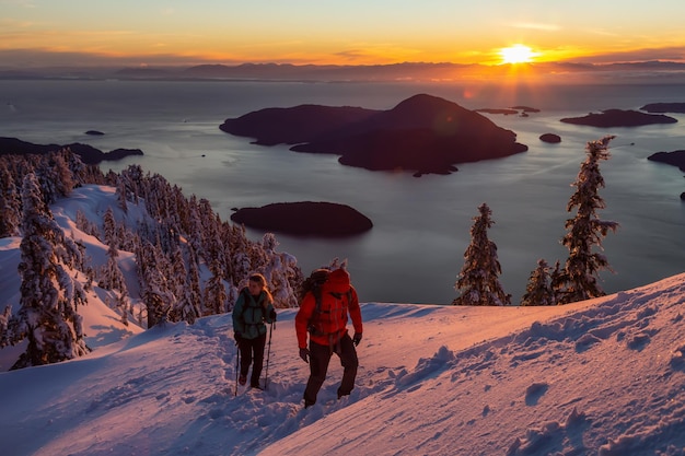 El hombre y la mujer que buscan aventuras están caminando hasta la cima de una montaña durante el atardecer de invierno