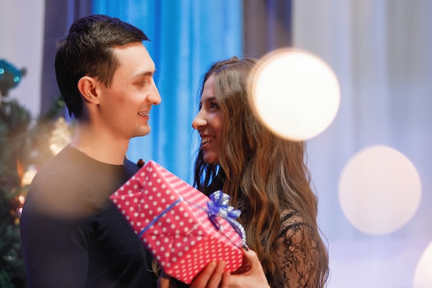 Hombre y mujer con un regalo cerca de un árbol de Navidad decorado.