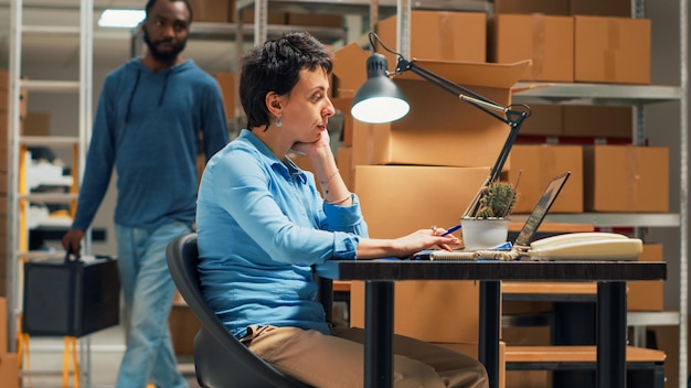 Hombre y mujer revisando el inventario y las existencias antes de enviar el pedido de mercancías, trabajando en el plan de negocios en el almacén. Propietario escribiendo datos en la computadora portátil, haciendo control de calidad. Disparo de mano.