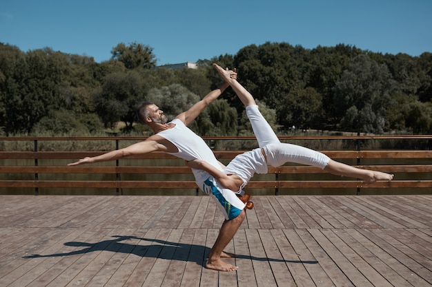 Hombre y mujer en ropa blanca practicando yoga avanzado al aire libre