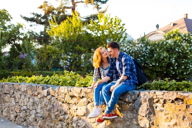 El hombre y la mujer con ropa cómoda, está sentado en una cerca de piedra y se miran con amor.