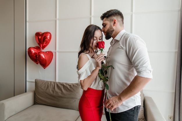 Hombre y mujer con una rosa roja en casa con globos en forma de corazón en el apartamento