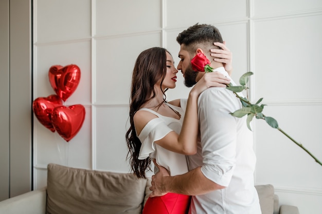 Hombre y mujer con una rosa roja en casa con globos en forma de corazón en el apartamento