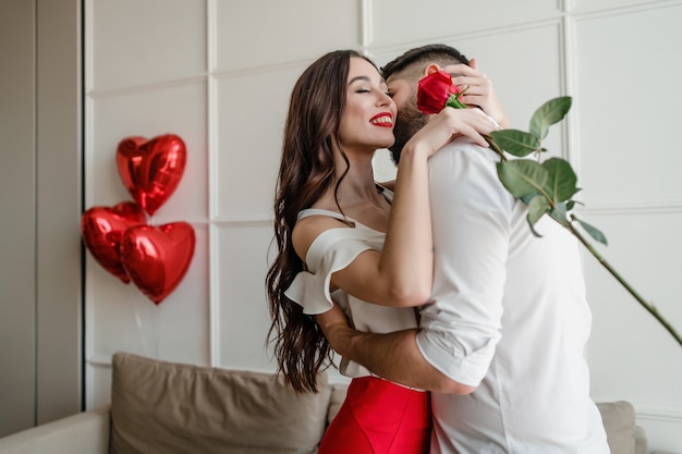 Hombre y mujer con una rosa roja en casa con globos en forma de corazón en el apartamento