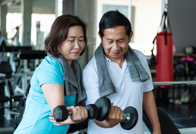 Hombre y mujer senior asiáticos ejercicio levantando pesas en el gimnasio. estilo de vida saludable para ancianos.