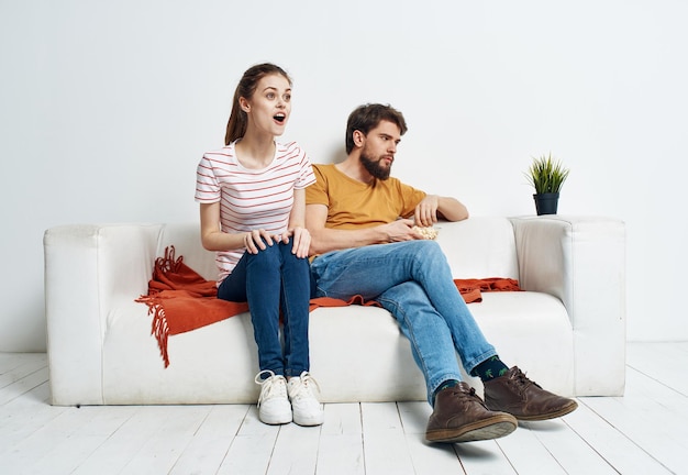 Un hombre y una mujer en un sofá blanco En una habitación luminosa un plato de palomitas de maíz y amigos una flor en una maceta