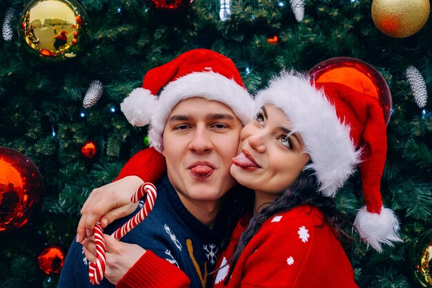 Hombre y mujer con sombreros de santa cerca del árbol de Navidad