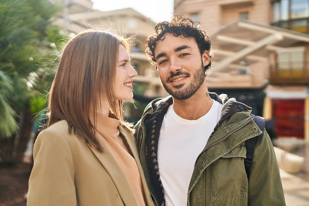 Hombre y mujer sonriendo confiados abrazándose unos a otros en la calle