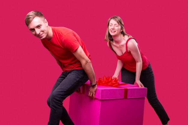 Hombre y mujer sonriente joven con expresión facial en camisetas rojas y jeans negros arrastrando la caja ...