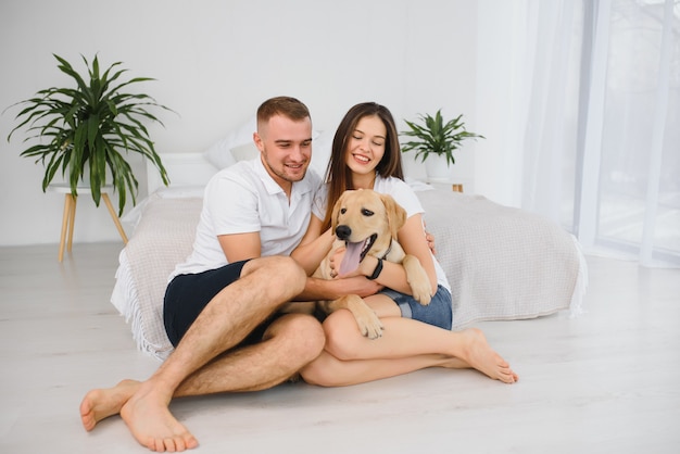 Hombre y mujer sonrientes sentados en el suelo en casa con su perro mascota