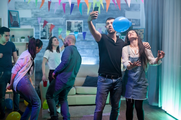 Hombre y mujer sonrientes tomando un selfie mientras se divierten en una fiesta.