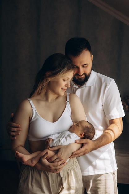 un hombre y una mujer sosteniendo a un bebé y el bebé está usando una camiseta blanca