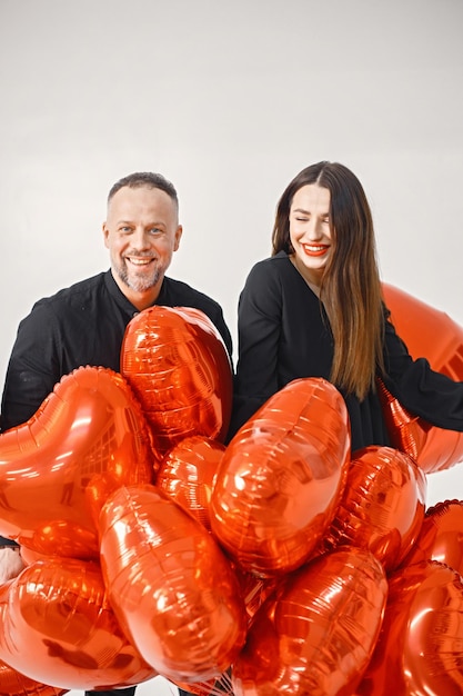 Hombre y mujer sosteniendo un montón de globos rojos en forma de corazón y posando en el estudio