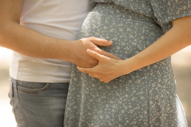 El hombre y la mujer sostienen un vientre embarazado, una madre embarazada con una camisa a cuadros y un esposo sostienen sus manos sobre su vientre, la pareja está esperando un hijo.