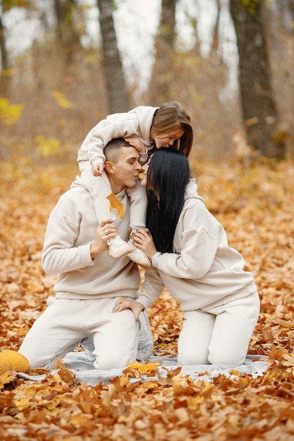 Hombre mujer y su niña sentada sobre una manta en el bosque de otoño Mujer morena y hombre juegan con su hija Familia vistiendo trajes deportivos beige