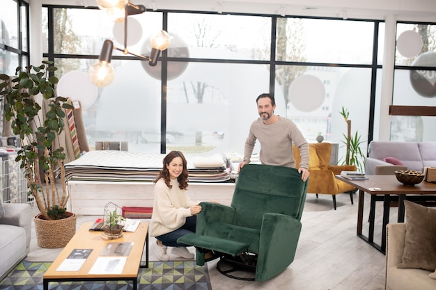 Hombre y mujer en suéteres ligeros mirando gran sillón verde