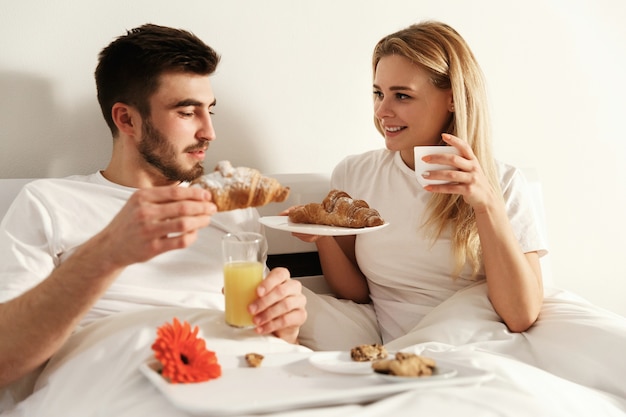 El hombre y la mujer tienen un delicioso desayuno francés acostado en la cama