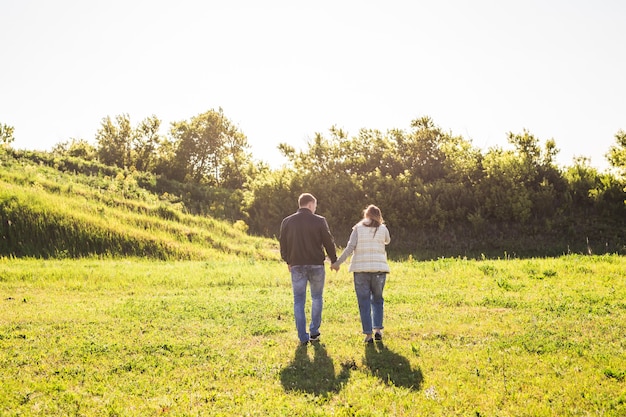 Foto hombre y mujer tomados de la mano y caminar sobre la naturaleza vista posterior