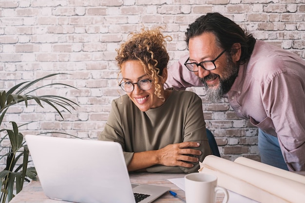 Hombre y mujer trabajando juntos en la oficina con proyectos de computadoras portátiles y papeles Estilo de vida de trabajo de comercio electrónico y negocios modernos Pareja feliz mirando pantalla de computadora y sonrisa Concepto de llamada de trabajo en línea