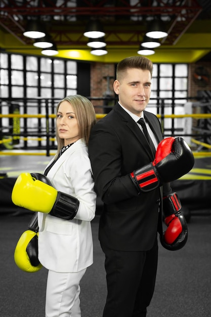 Un hombre y una mujer con traje y guantes de boxeo se paran frente al ring de espaldas el uno al otro.