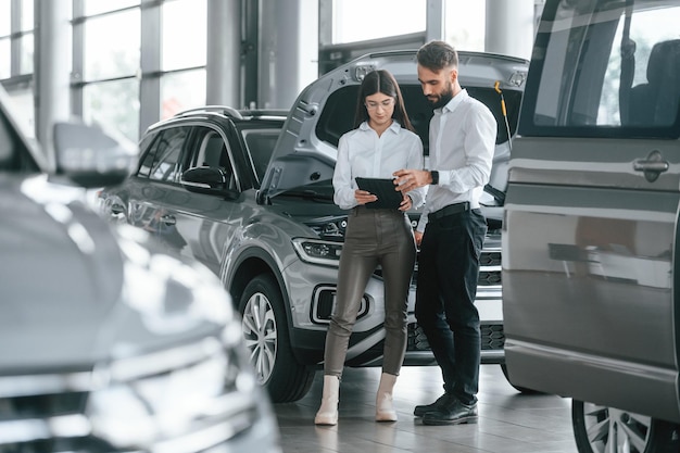 El hombre con la mujer vestida de blanco están juntos en el concesionario de automóviles