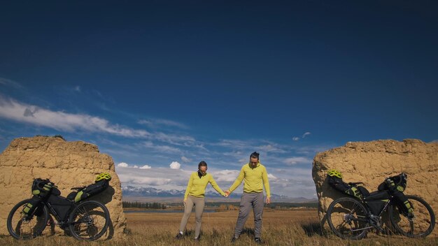 El hombre y la mujer viajan en cicloturismo de terreno mixto con bikepacking Las dos personas viajan con bolsas de bicicleta Arco de piedra cubierto de nieve de montaña