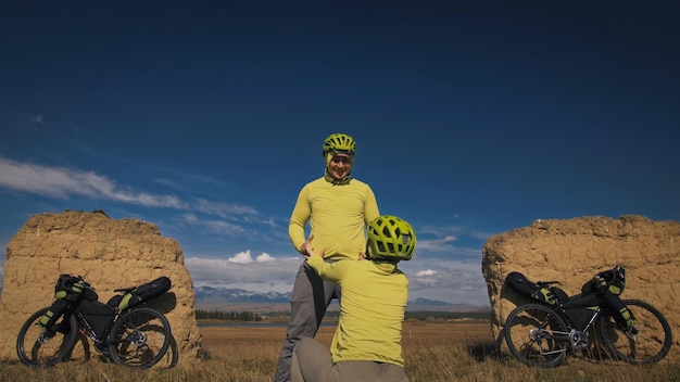 El hombre y la mujer viajan en cicloturismo de terreno mixto con bikepacking Las dos personas viajan con bolsas para bicicletas Ropa deportiva deportiva en colores verdes y negros Arco de piedra cubierto de nieve de montaña