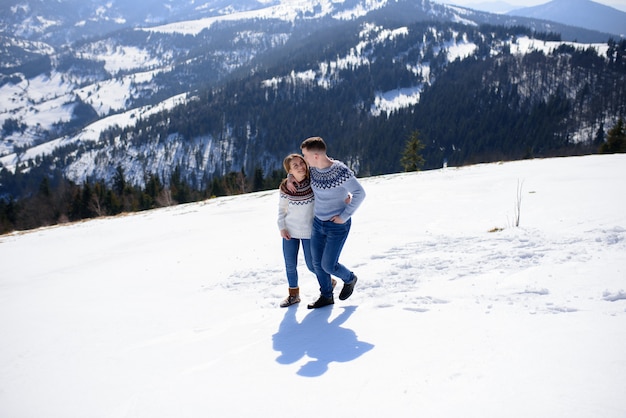 Hombre y mujer vistiendo ropa tejida abrazando en montaña nevada.