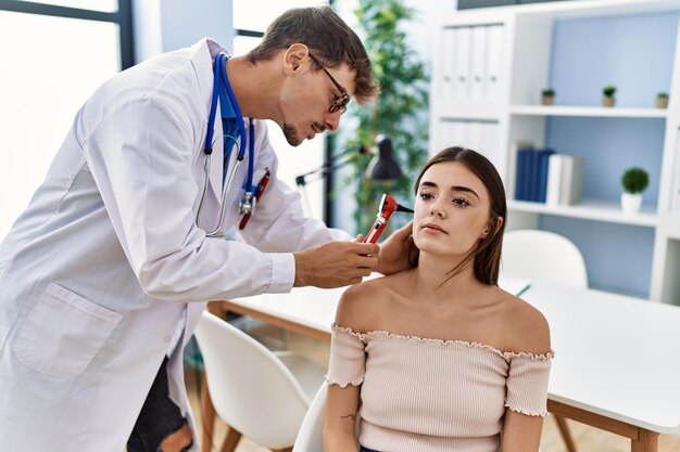 Foto hombre y mujer vistiendo uniforme médico auscultando la oreja usando otoscopio en la clínica