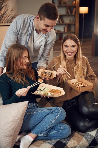 Foto hombre con mujeres amigos están sentados en el interior de la casa y comiendo sushi juntos