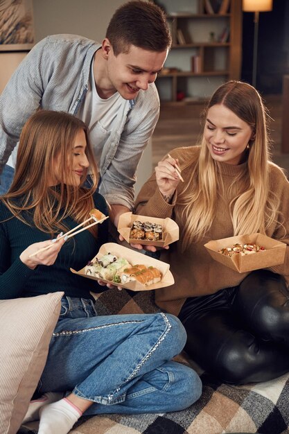 Foto hombre con mujeres amigos están sentados en el interior de la casa y comiendo sushi juntos