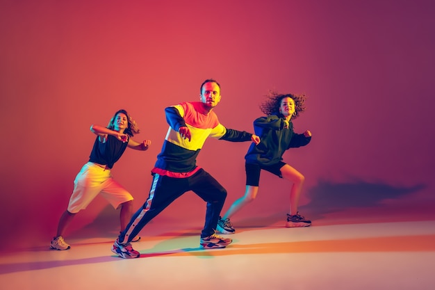 Hombre y mujeres con estilo bailando hip-hop en ropa brillante sobre fondo degradado