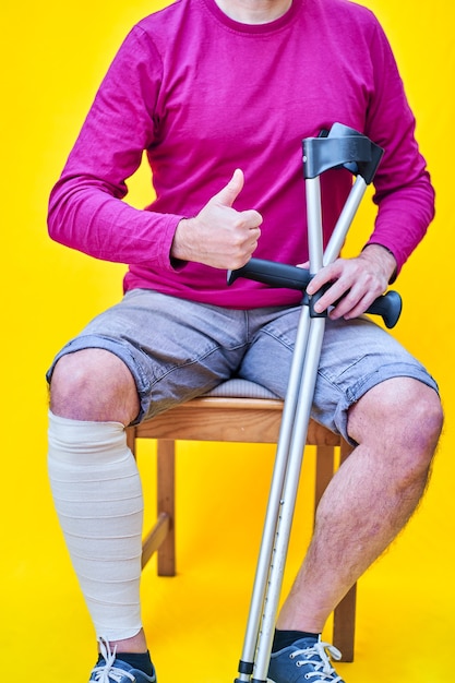 hombre con muletas, jeans y camisa morada sentado en una silla con el pulgar hacia arriba.