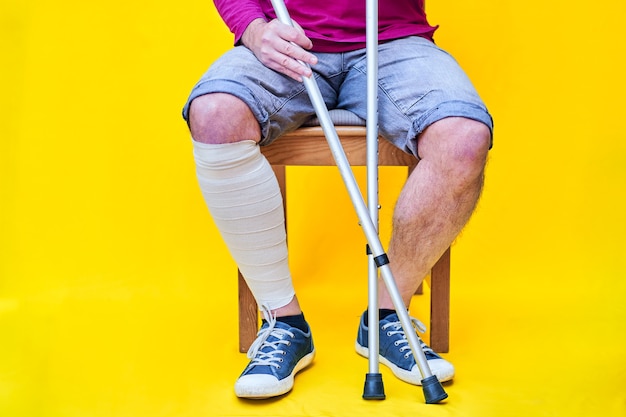 Foto hombre con muletas, jeans y camisa morada sentado en una silla.