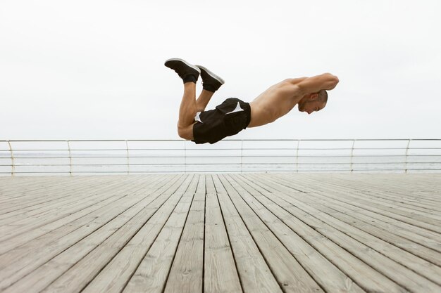 Foto hombre musculoso acrobático en vuelo sobre el suelo en la playa