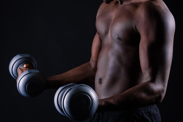 Hombre musculoso africano aislado con pesas sobre fondo oscuro de estudio fuerte chico negro sin camisa
