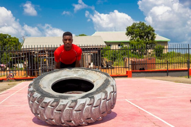 Hombre musculoso africano trabajando en el gimnasio volteando neumáticos grandes