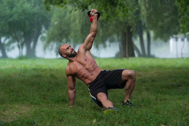 Hombre musculoso arrodillado haciendo ejercicio con pesas rusas